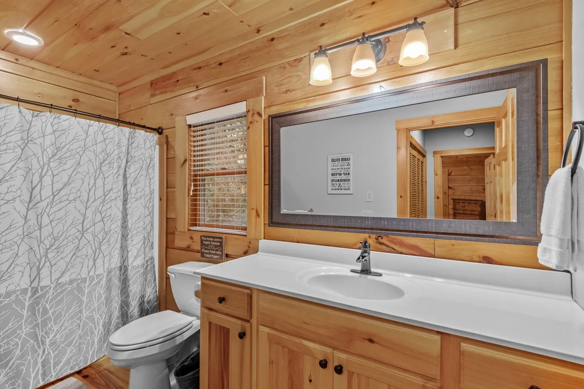 A modern, updated bathroom with wooden cabinetry, a large mirror, and a shower with a nature-inspired curtain. The inviting design features warm natural wood and soft lighting, creating a space ideal for self-care routines and post-adventure refreshment.