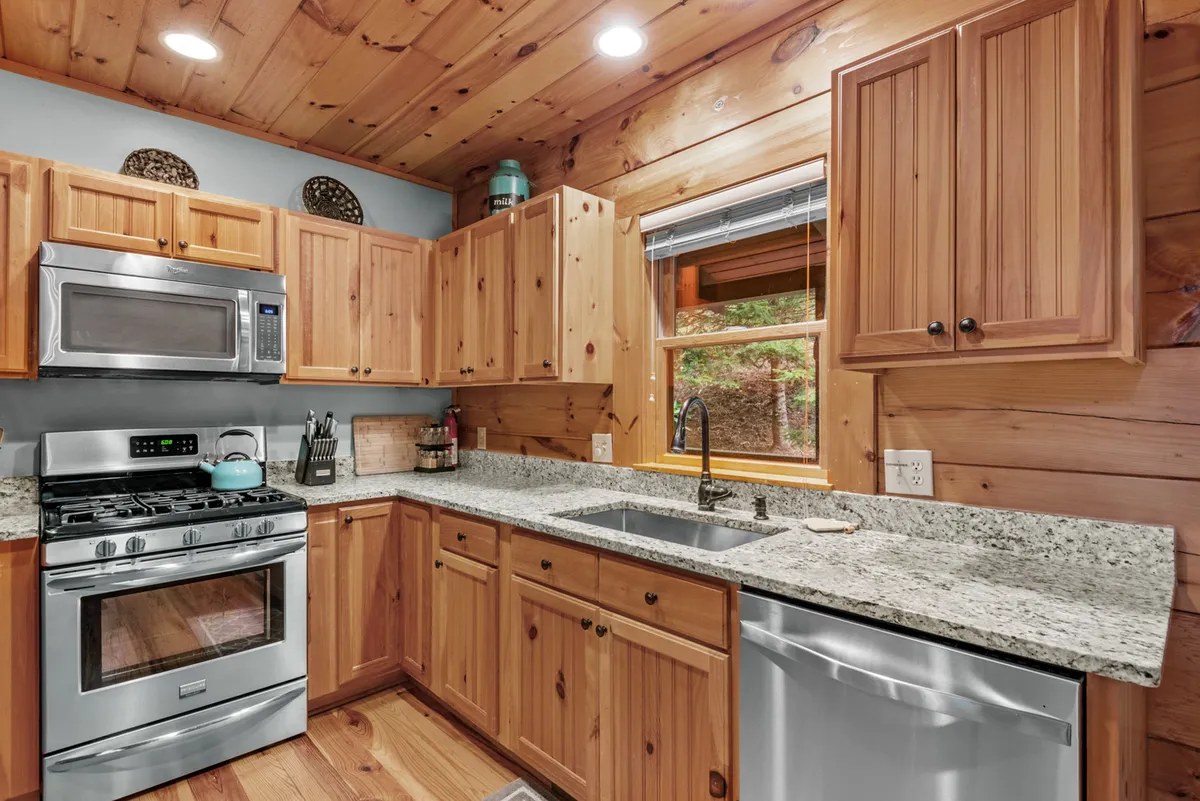 A close-up view of the kitchen highlights granite countertops, upgraded stainless steel appliances—including a gas stove—and rich wooden cabinetry. Sunlight streams through a window, creating a welcoming and homey ambiance ideal for family meal prep and casual conversations.