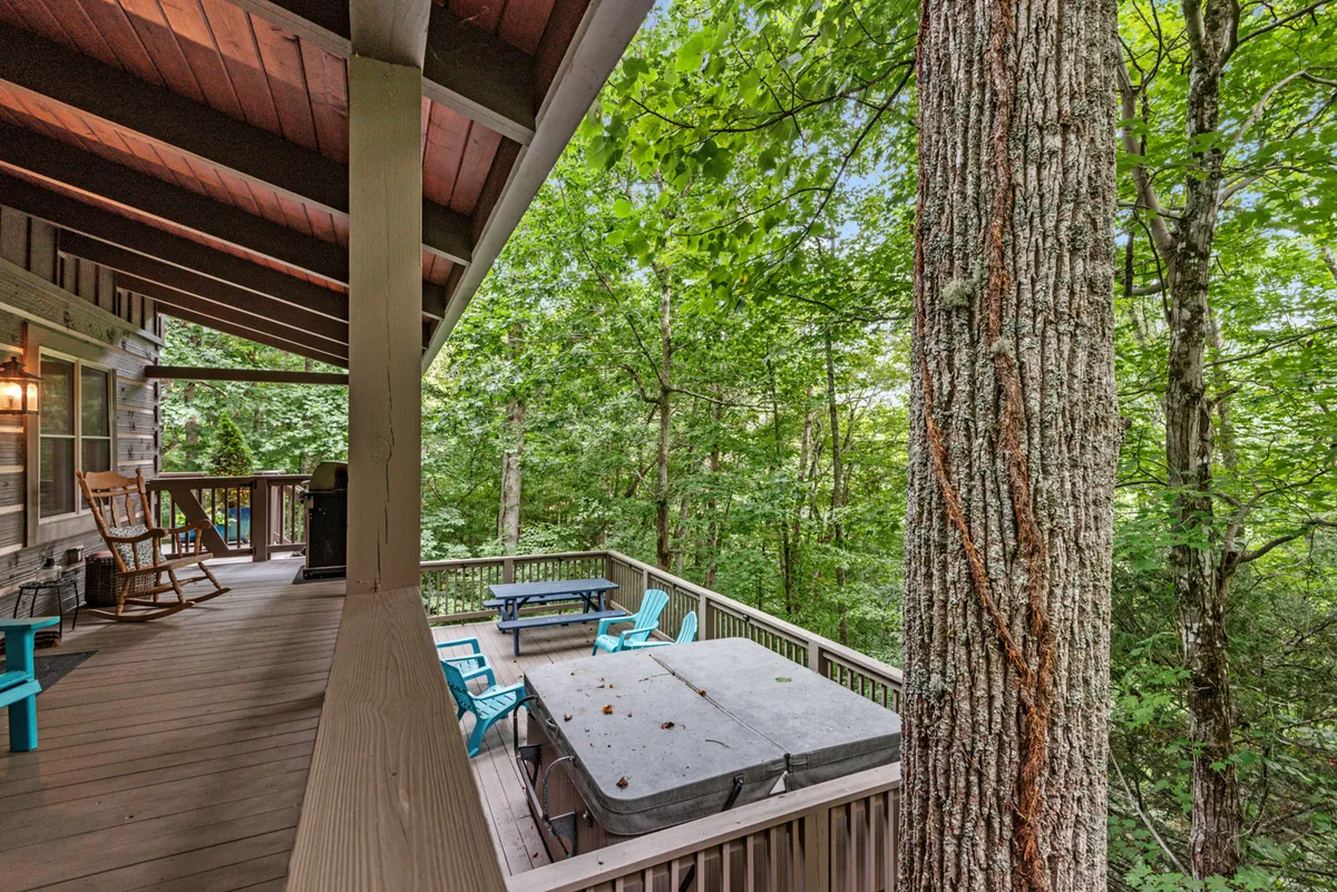 A wide wooden deck nestled among tall trees, furnished with Adirondack chairs and a table under cover. The view provides a sense of space for outdoor relaxation, dining, or simply taking in the forested landscape.